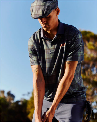 A man wearing a blue and green plaid polo shirt and matching flat cap.