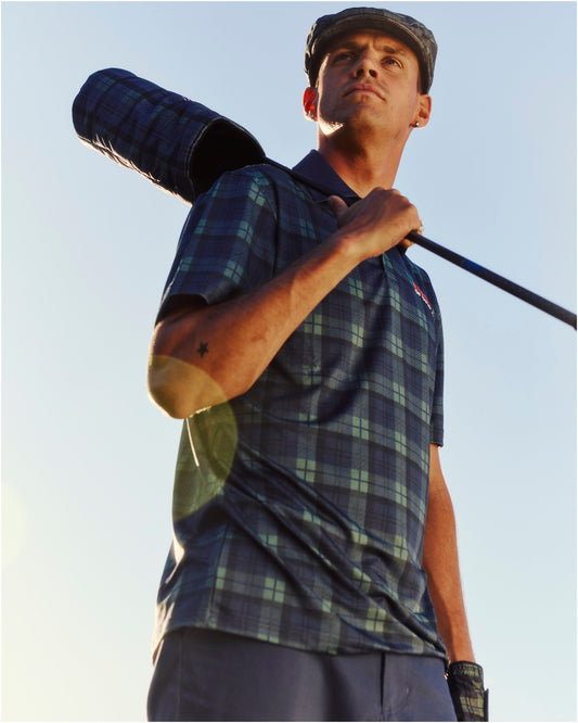 A man wearing a blue and green plaid polo shirt, cap, and holding a matching driver headcover.