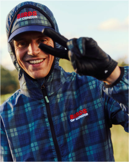 A man wearing a blue and green plaid jacket with a matching hooded cap, featuring embroidered branding.