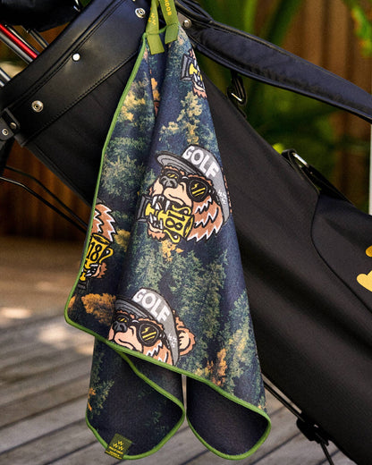 Black golf towel hanging from a bag, featuring a printed bear motif and a green trim.