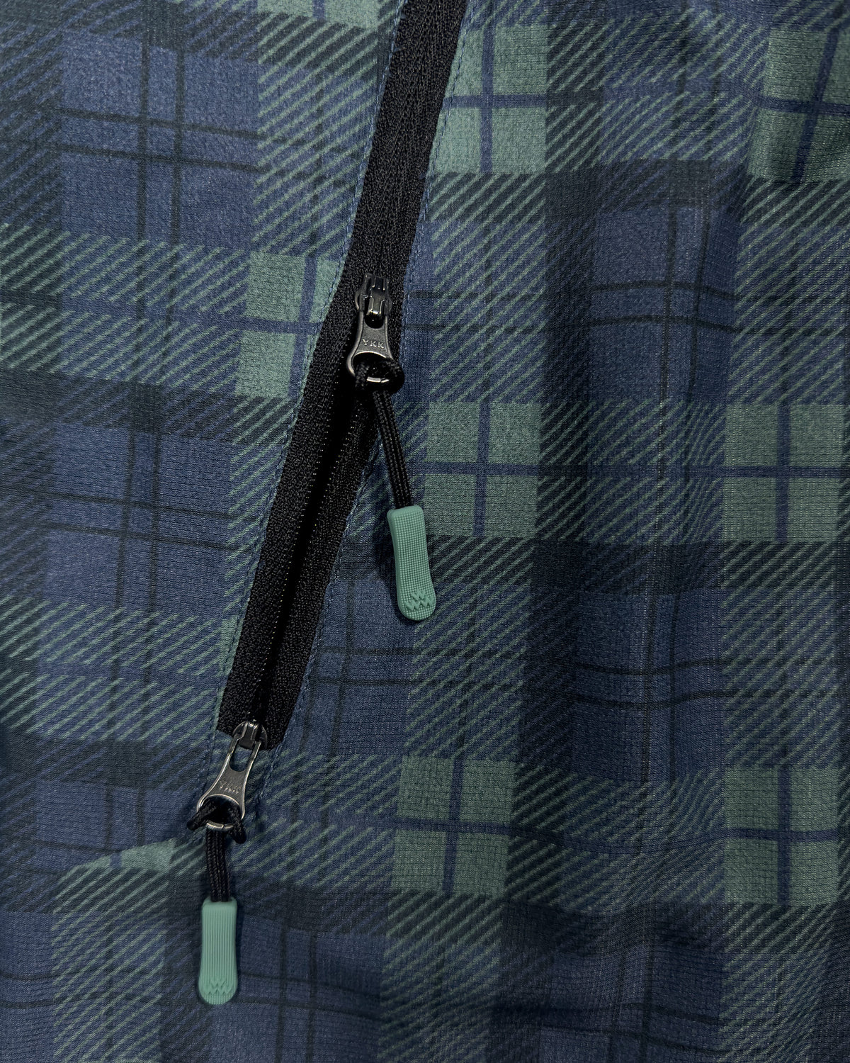Detail of a blue and green plaid jacket with black zippered pockets and branded zip pulls.