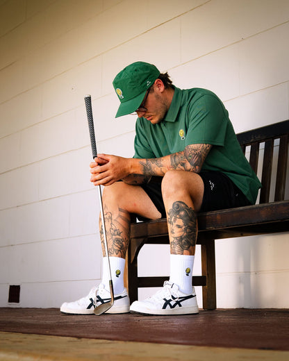 A man wearing a green polo shirt and matching green cap, sitting on a wooden bench holding a golf club.