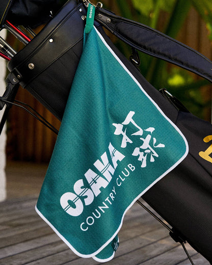 Alpine green golf towel hanging from a black golf bag, featuring a white graphic print and a green nylon loop.