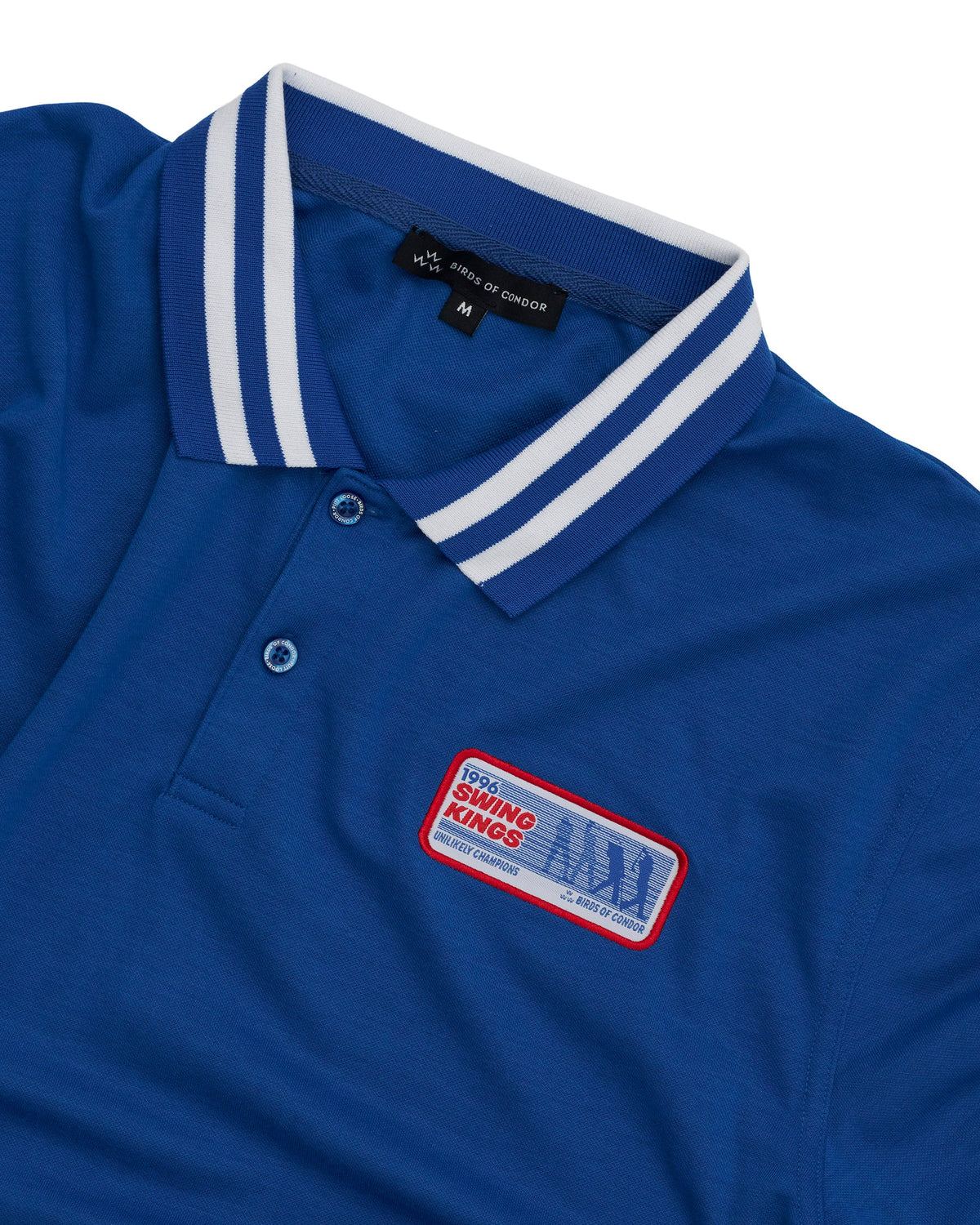 Detail of a blue polo shirt featuring a striped collar, a two-button placket, and a Swing Kings patch.