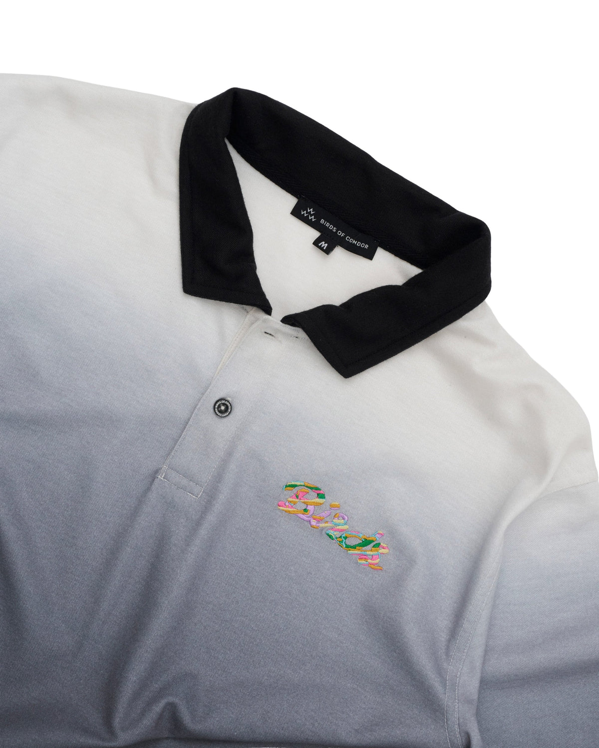 Detail of a black gradient polo shirt featuring a black collar and a colourful printed chest design.