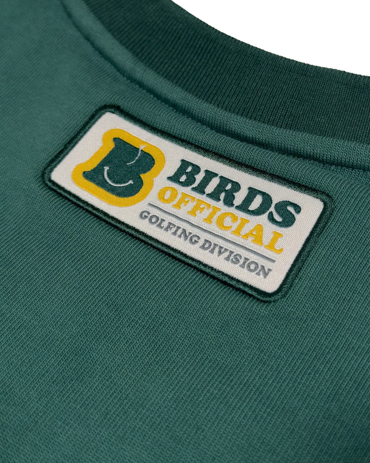 Detail of a green cotton sweater featuring a rectangular patch with Birds Official Golfing Division text.