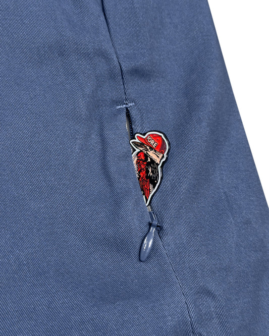 Detail of blue cotton pants showing a zipper pocket containing a bird graphic with a red hat.