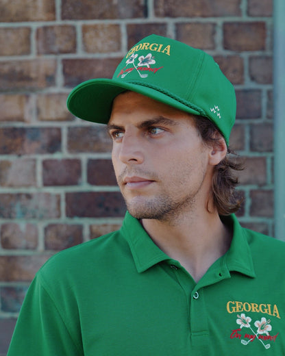 A man wearing a green snapback hat featuring a yellow and white floral golf club design.