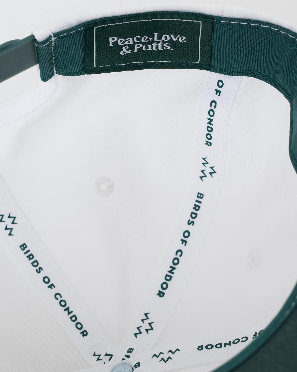 Detail of a white snapback's interior, showing green inner taping with Peace, Love & Putts lettering.