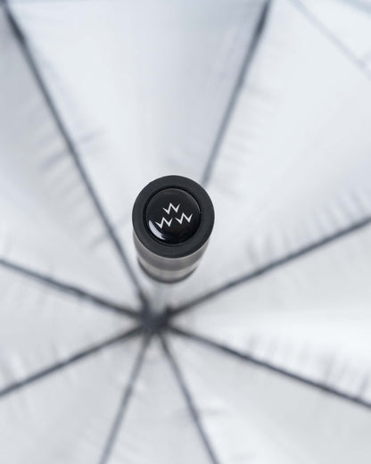 Detail of a blue and green plaid umbrella featuring a branded pop button with a three-prong crown logo.