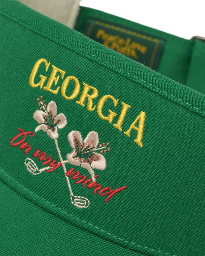 Detail of a Masters Green cotton visor featuring embroidered yellow text and crossed flower and golf club graphics.