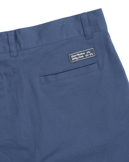 Detail of blue cotton shorts featuring belt loops, a welt pocket, and a dark woven brand label.
