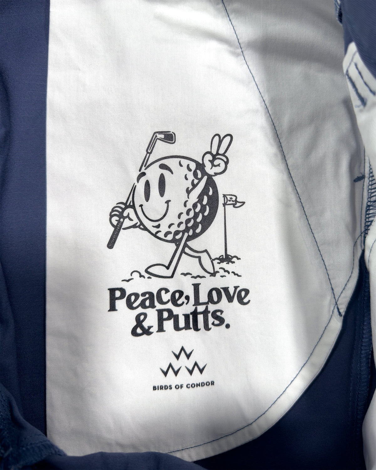 Detail of blue shorts with a printed inner pocket featuring a smiling golf ball holding a club.