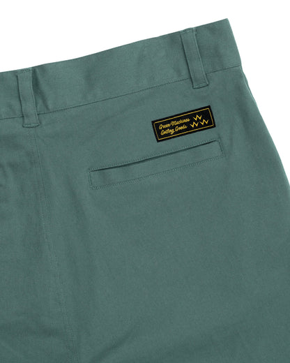 Detail of khaki green shorts featuring a welt pocket and a black logo patch above it.