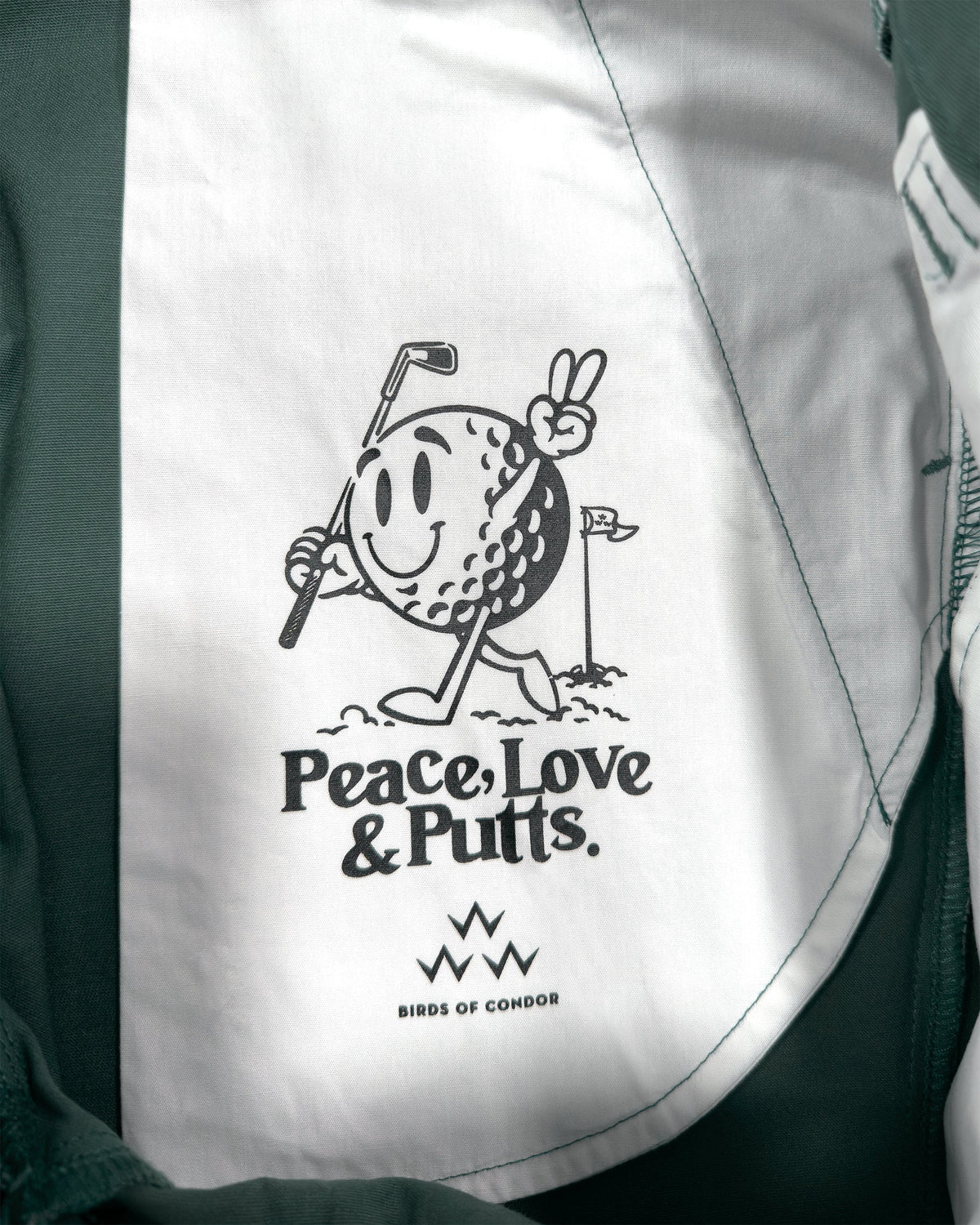 Detail of khaki green shorts with a white printed inner pocket featuring a smiling golf ball holding a club.