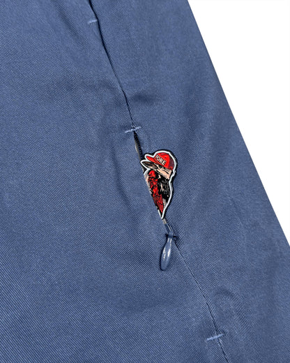 Detail of blue shorts with a zipped pocket featuring a red bird graphic pull.