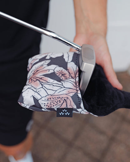 A person holding an azalea-print mallet headcover with a black inner lining and a putter inserted inside.