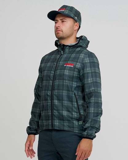A man wearing a blue and green plaid shell jacket with an embroidered front logo, black zip, and matching cap.