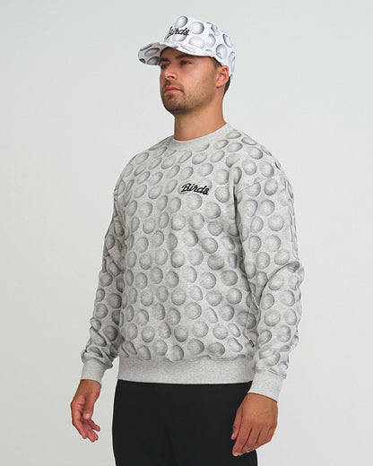 A man wearing a gray sweater with an all-over golf ball graphic and a matching cap, paired with black pants.