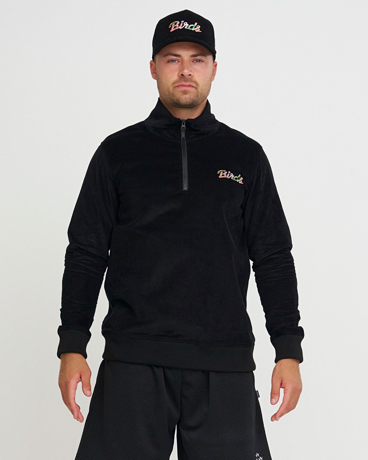 Man wearing a black hoodie and cap with 'Birds' branding on a light gray background
