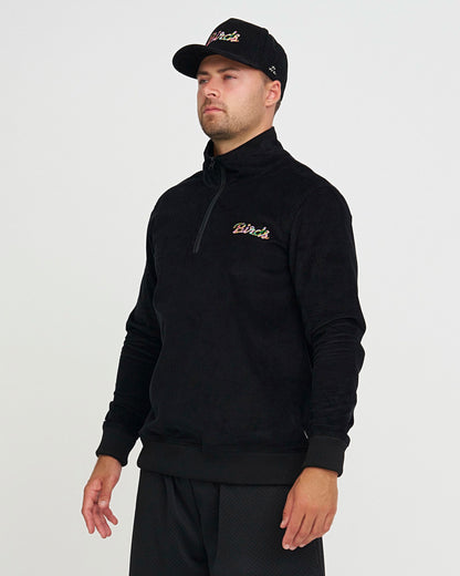 Man wearing a black quarter-zip sweatshirt with a logo on a light gray background