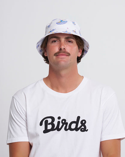 A man wearing a white cotton bucket hat with an all-over blue and yellow graphic motif.