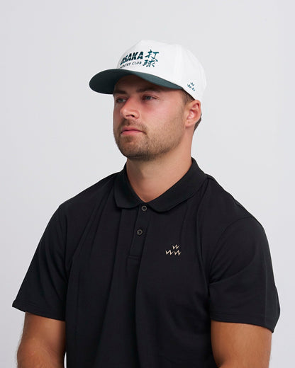 A man wearing a white snapback with a green brim and an Osaka Country Club embroidery on the front.