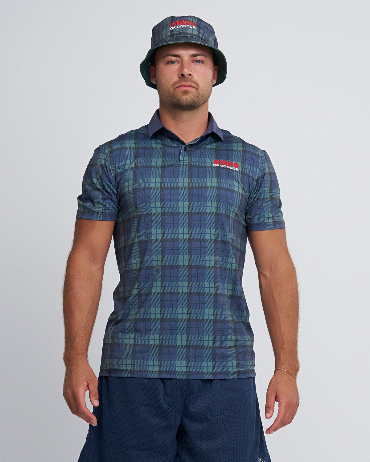 A man wearing a blue and green plaid polo shirt and matching bucket hat, with a red chest logo.