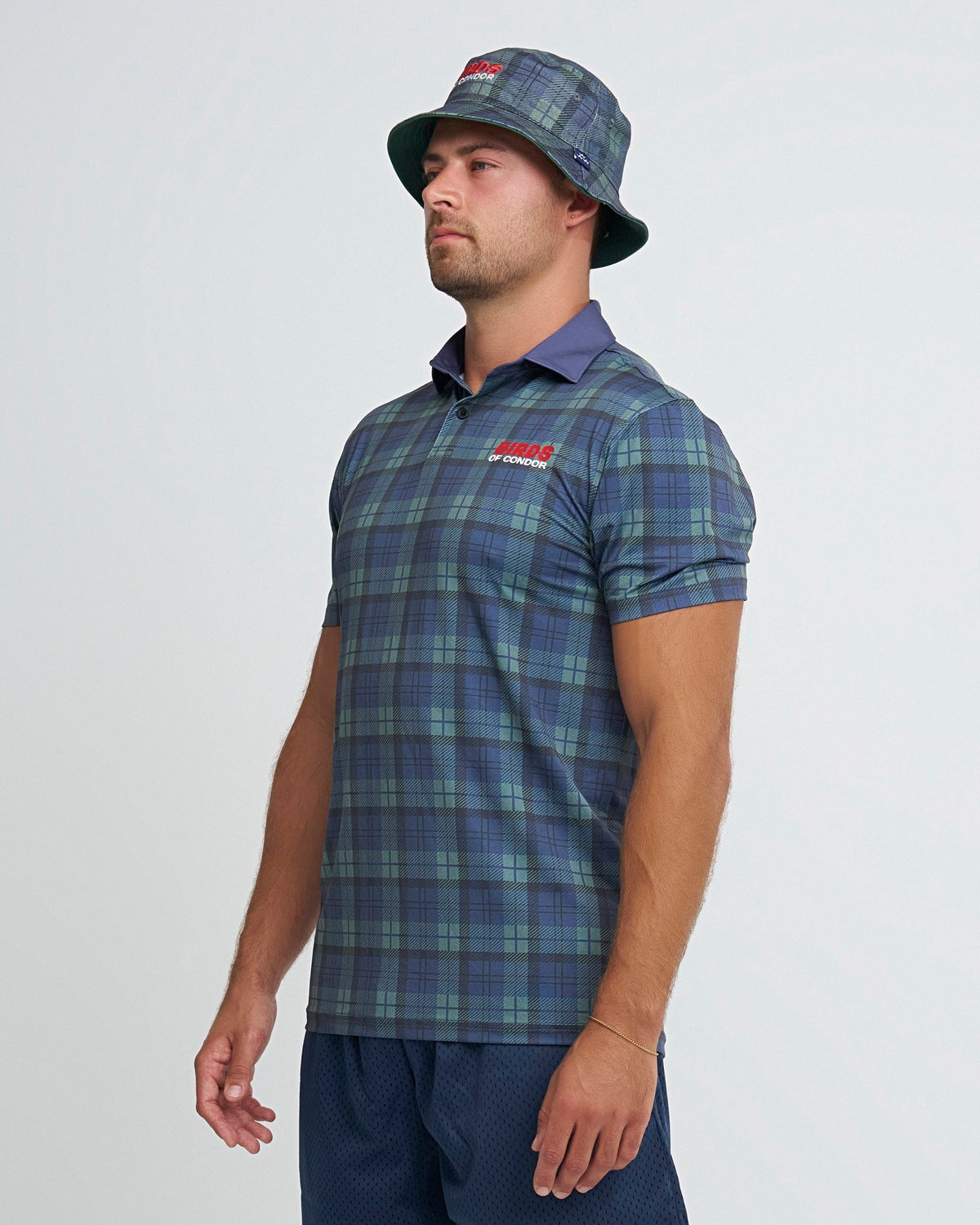 A man wearing a blue and green plaid polo shirt with a red logo on the chest and matching bucket hat.