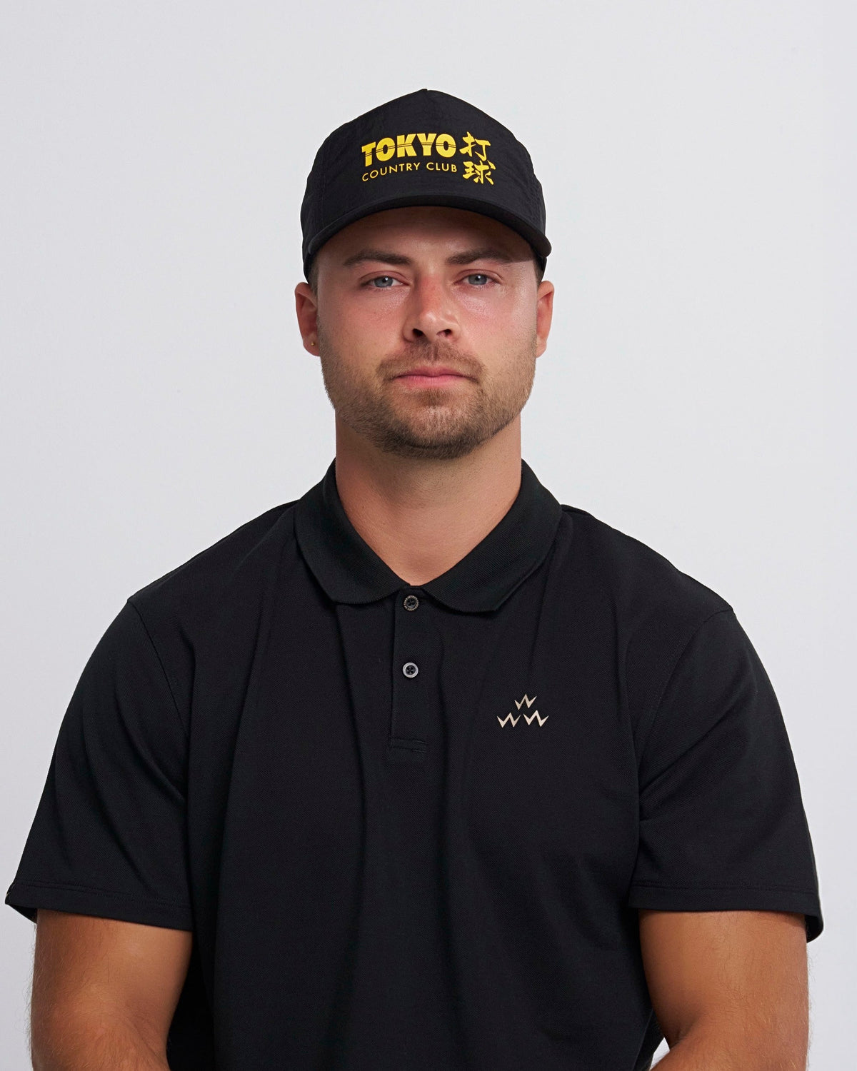 A man wearing a black snapback cap featuring yellow Tokyo Country Club text and Japanese characters.