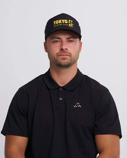 A man wearing a black snapback cap featuring yellow Tokyo Country Club text and Japanese characters.