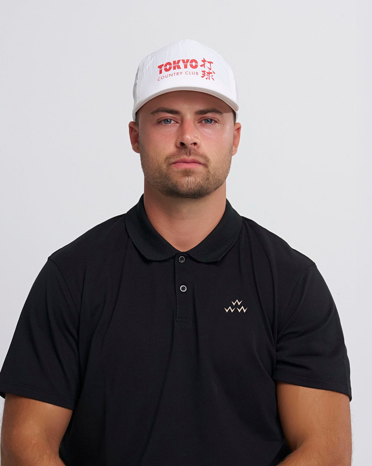 A man wearing a white snapback cap featuring red Tokyo Country Club lettering on the structured front.
