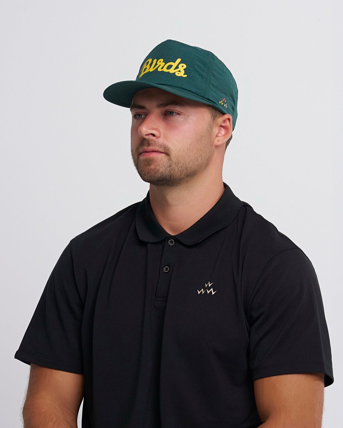 A man wearing an alpine green nylon snapback cap with yellow script print and a curved brim.