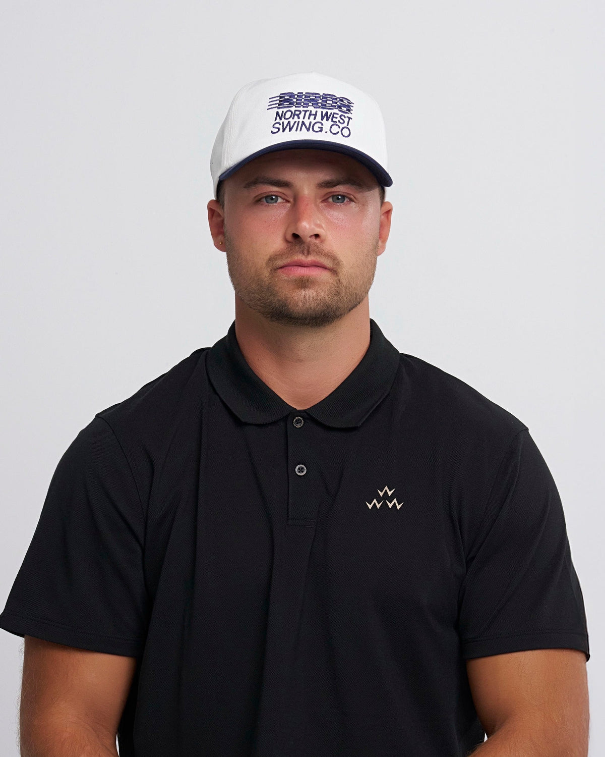 A man wearing a white snapback cap with a navy brim and blue North West Swing Co. embroidery.