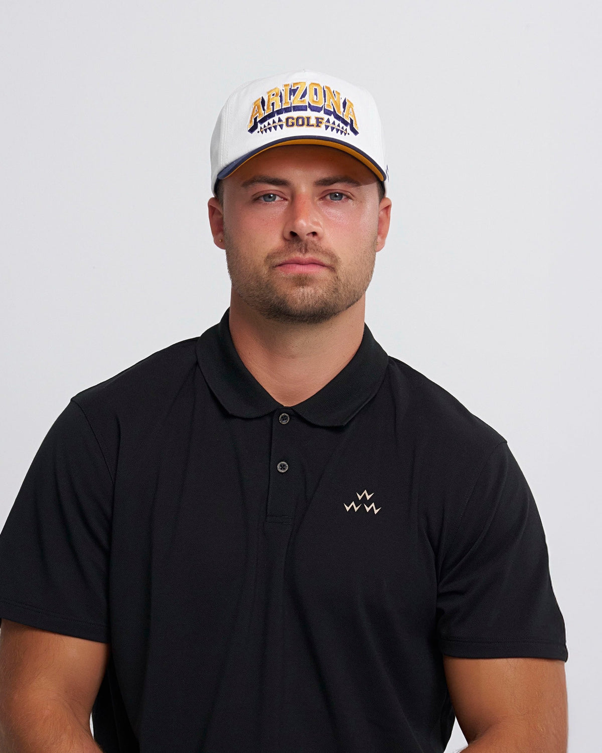 A man wearing a white snapback with a navy brim and yellow and blue Arizona Golf text embroidery.
