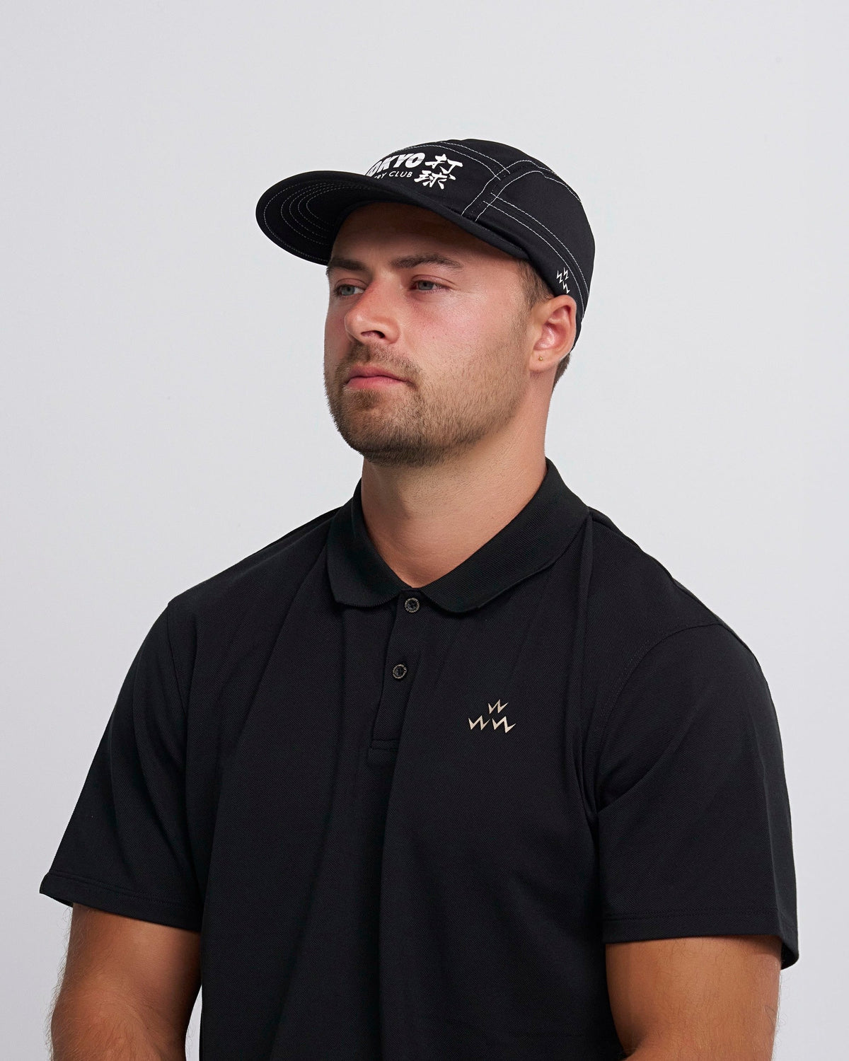A man wearing a black sports cap with white contrast stitching and a printed front graphic.