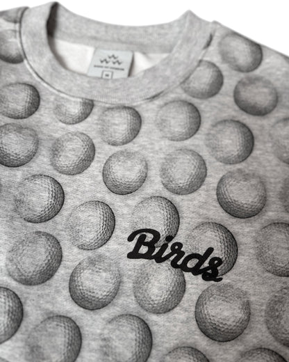 Detail of a gray sweater featuring an all-over golf ball print and a black cursive Birds chest logo.