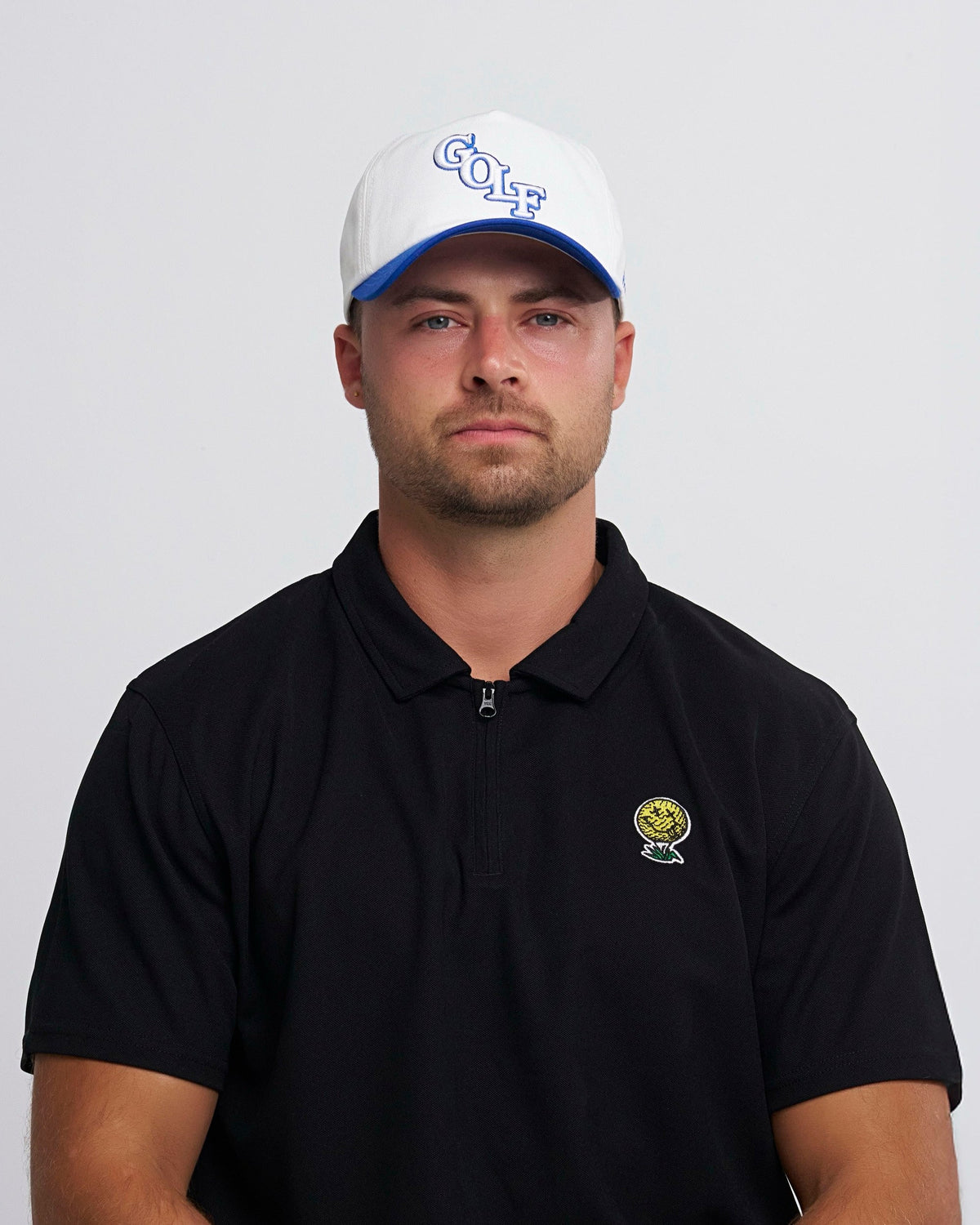 A man wearing a white snapback hat with blue brim and a GOLF text logo on the front.