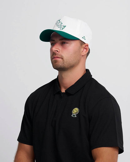 Man wearing a black polo shirt with a neverfind yellow golf ball logo and a white cap with green brim and logo on a gray background