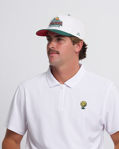 A man wearing a white snapback hat with a green curved brim and a colorful Arizona Desert Golf Society graphic.