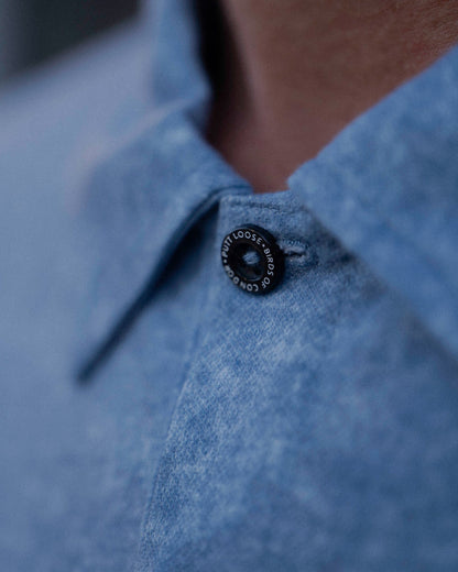 Detail of an acid blue polo shirt with a black branded button at the neckline.