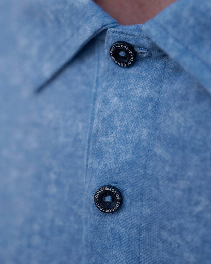 Detail of an acid blue polo shirt featuring black branded tonal buttons along the placket.