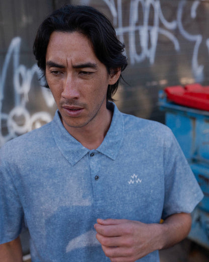 A man wearing an acid blue polo shirt featuring a white Triple Eagle logo on the chest.