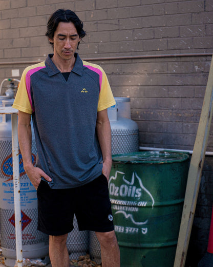 A man wearing a black polo shirt with yellow and pink sleeves, a V-neck, and a small triple eagle logo.