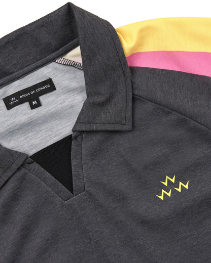 Detail of a black polo shirt with yellow and pink shoulder stripes and a yellow triple eagle logo.