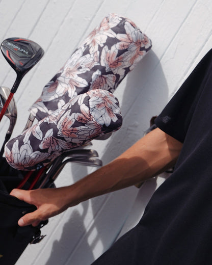 A person in a black shirt holding a golf bag with azalea print headcovers.
