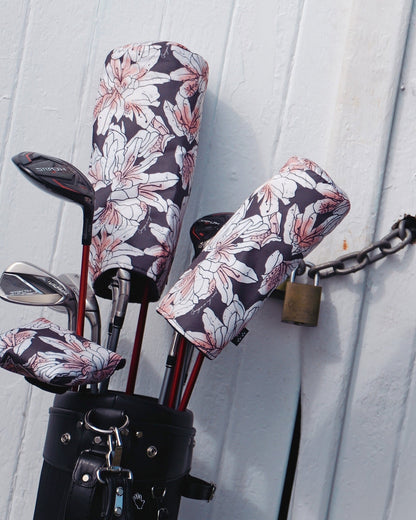 Golf club headcovers in azalea print with large pink flowers, fitted onto clubs in a black bag.