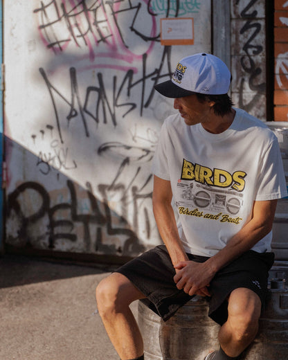 A man wearing a white t-shirt featuring a retro boombox graphic and yellow text across the chest.