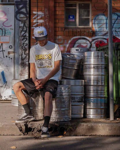A man wearing a white t-shirt featuring a retro print graphic, black shorts, and a matching cap.