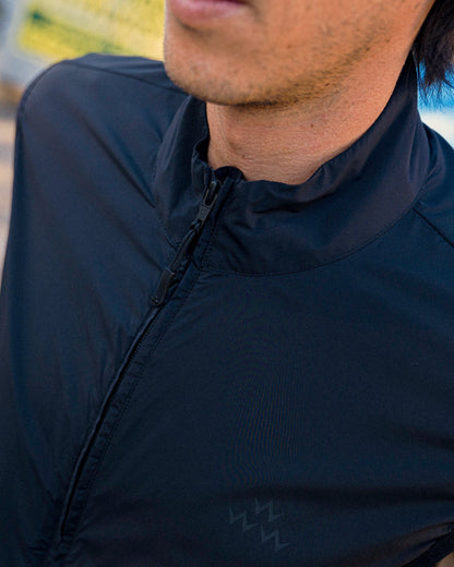 A person wearing a black shell vest with a funnel neck and a central front zipper.